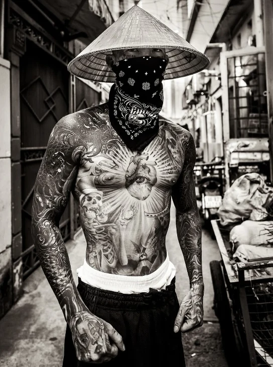 Tattooed Asian Barrio brother wearing the black Bandana and a traditional conical hat in an alley